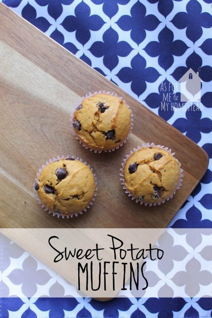 Three chocolate chip sweet potato muffins on a wooden cutting board, which rests on a blue and white placemat